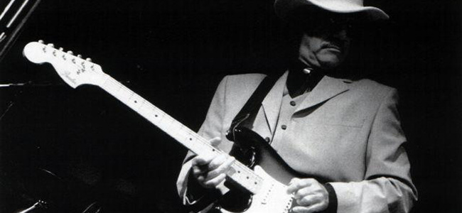 Pete on stage in a pale suit and hat, playing a Stratocaster, black and white